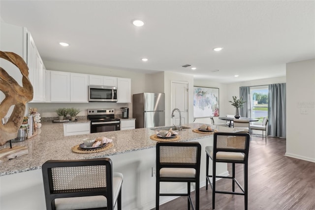 16307 Alcira Cir, Punta Gorda, FL 33955 - kitchen with stainless steel appliances, white cabinets, light stone countertops, wood finished floors, and a peninsula