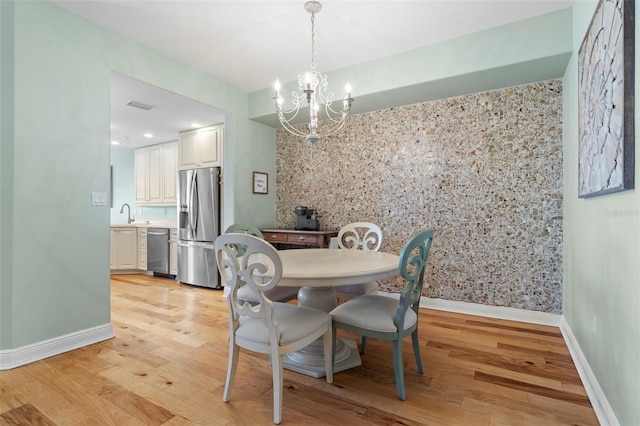 dining area with light hardwood / wood-style flooring, a notable chandelier, and sink