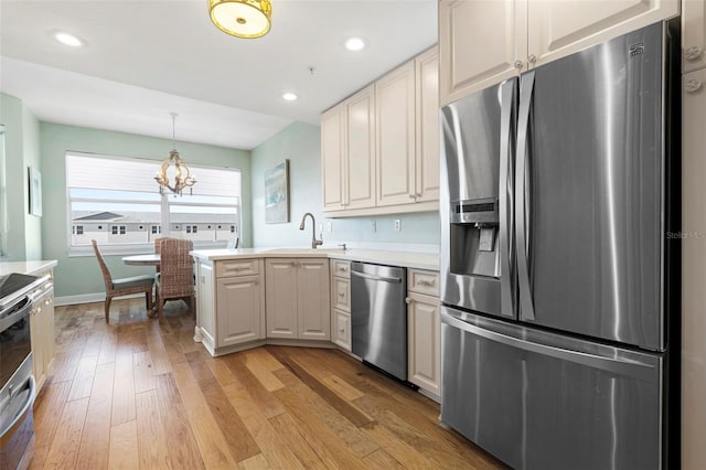 kitchen featuring stainless steel appliances, kitchen peninsula, a chandelier, sink, and light hardwood / wood-style flooring