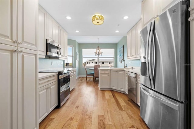 kitchen featuring white cabinetry, appliances with stainless steel finishes, pendant lighting, an inviting chandelier, and light hardwood / wood-style floors