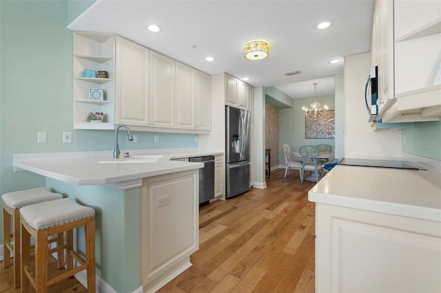 kitchen with white cabinetry, sink, kitchen peninsula, appliances with stainless steel finishes, and light wood-type flooring