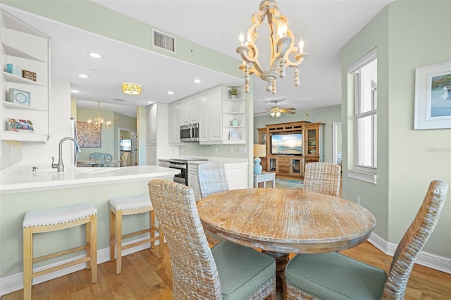 dining area featuring sink, ceiling fan with notable chandelier, and light hardwood / wood-style flooring