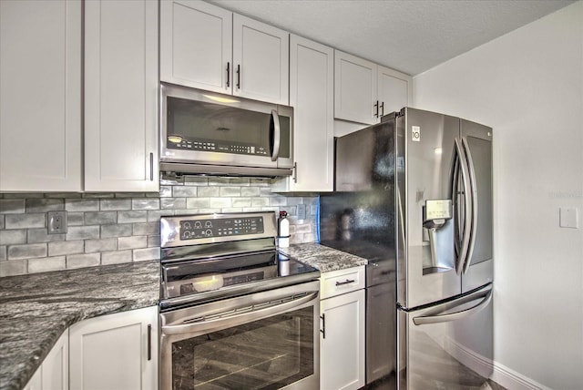 kitchen with white cabinets, appliances with stainless steel finishes, dark stone counters, and backsplash