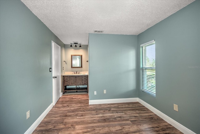 unfurnished bedroom featuring a textured ceiling, sink, hardwood / wood-style floors, and ensuite bath