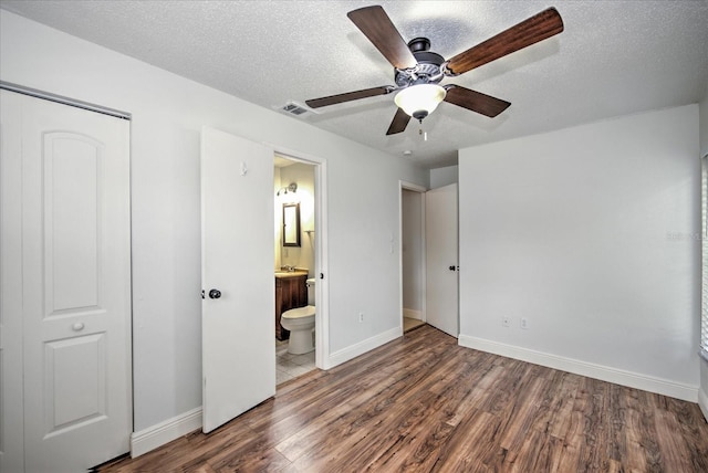 unfurnished bedroom with ceiling fan, a textured ceiling, dark hardwood / wood-style floors, and ensuite bath