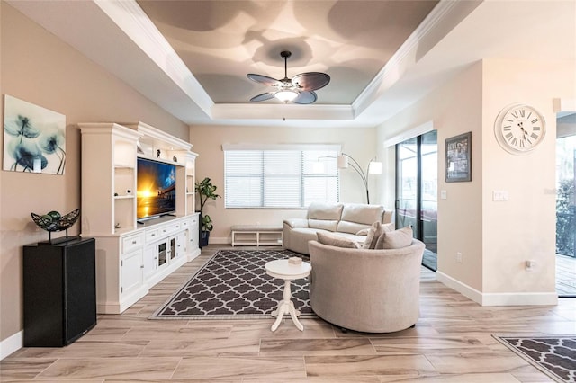 living room with light hardwood / wood-style floors, ceiling fan, crown molding, and a tray ceiling