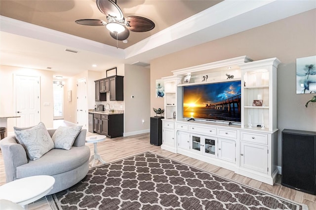 living room with ceiling fan, sink, light wood-type flooring, and a tray ceiling