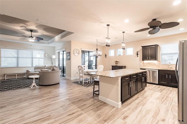 kitchen featuring appliances with stainless steel finishes, light stone counters, a kitchen breakfast bar, a kitchen island, and pendant lighting