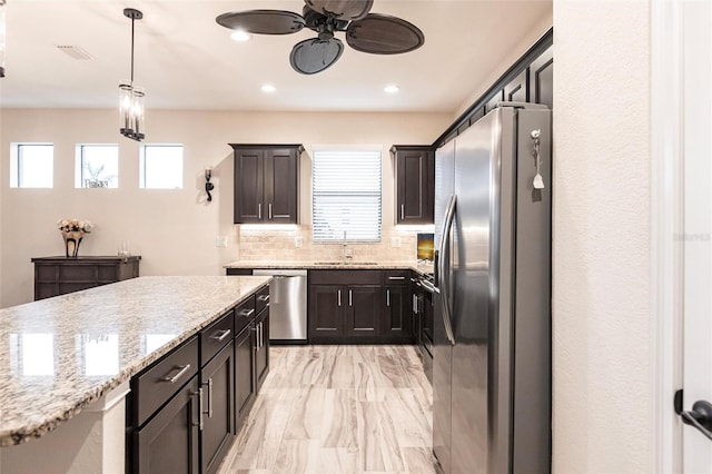 kitchen featuring stainless steel appliances, light stone counters, sink, tasteful backsplash, and pendant lighting