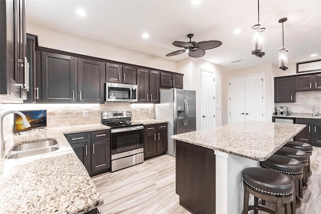 kitchen with dark brown cabinetry, sink, appliances with stainless steel finishes, hanging light fixtures, and a kitchen island