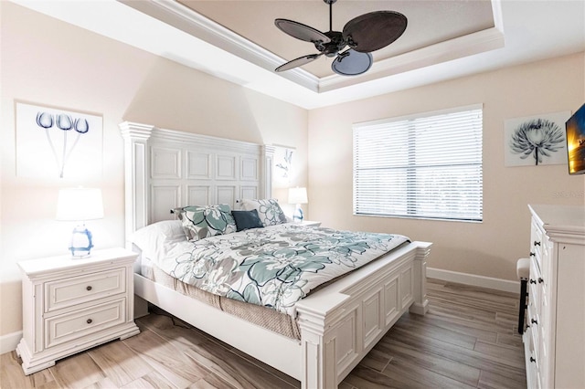 bedroom with light wood-type flooring, ceiling fan, and a raised ceiling