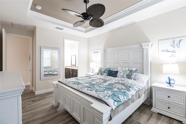 bedroom featuring dark hardwood / wood-style floors, a tray ceiling, ceiling fan, and ensuite bath