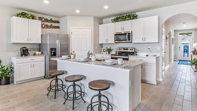 kitchen featuring a breakfast bar, a kitchen island with sink, sink, appliances with stainless steel finishes, and white cabinetry