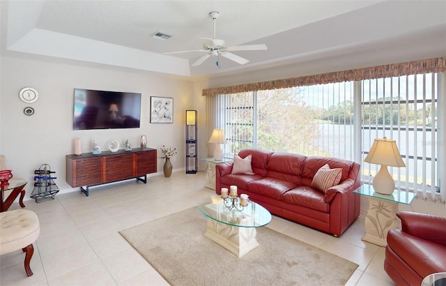 living room featuring a raised ceiling, ceiling fan, and tile patterned flooring