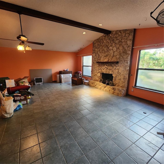 unfurnished living room with a wealth of natural light, ceiling fan, a textured ceiling, and vaulted ceiling with beams