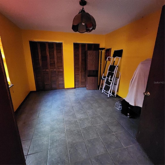 unfurnished bedroom with dark tile patterned floors, a textured ceiling, and two closets