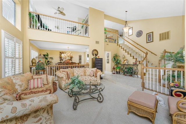 living room with a towering ceiling, ceiling fan with notable chandelier, and light carpet