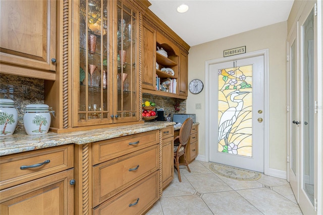 interior space featuring light tile patterned flooring, built in desk, backsplash, and light stone counters