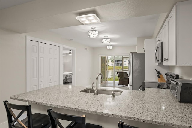 kitchen with stainless steel appliances, sink, a kitchen breakfast bar, light stone countertops, and white cabinets