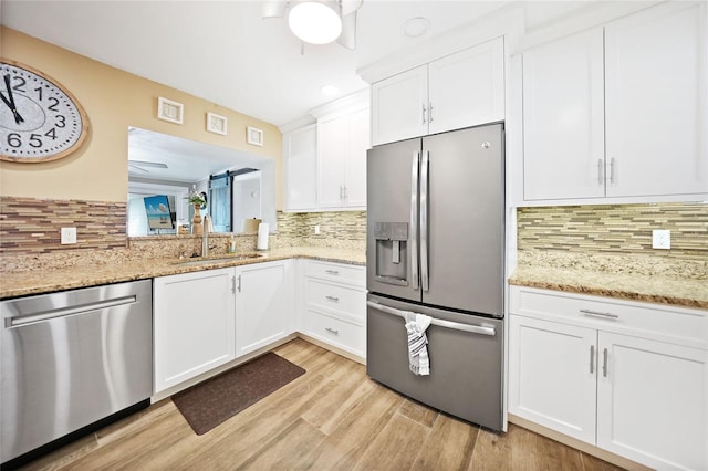 kitchen featuring stainless steel appliances, light wood-type flooring, white cabinetry, decorative backsplash, and sink