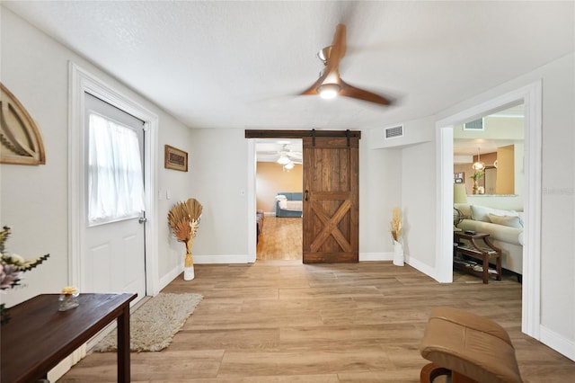 foyer entrance with a barn door, ceiling fan, and light wood-type flooring