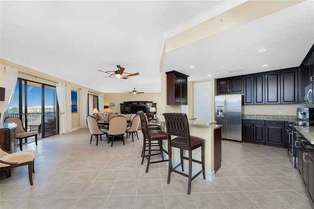 kitchen featuring a breakfast bar, ceiling fan, light stone countertops, ornamental molding, and stainless steel appliances