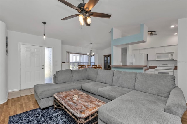 living room with ceiling fan with notable chandelier, lofted ceiling, and light hardwood / wood-style flooring