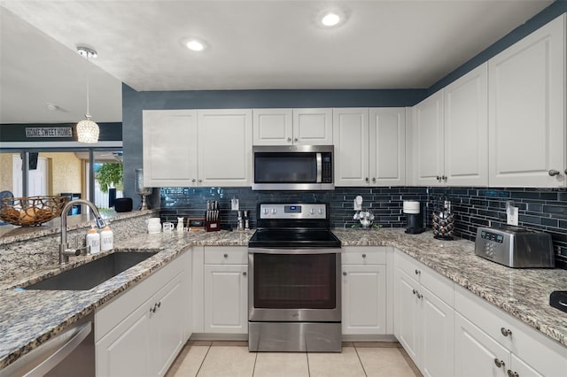 kitchen with light stone counters, appliances with stainless steel finishes, light tile patterned floors, sink, and white cabinets