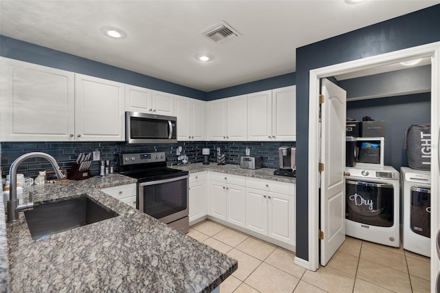 kitchen with stainless steel appliances, dark stone counters, white cabinets, sink, and washer and clothes dryer