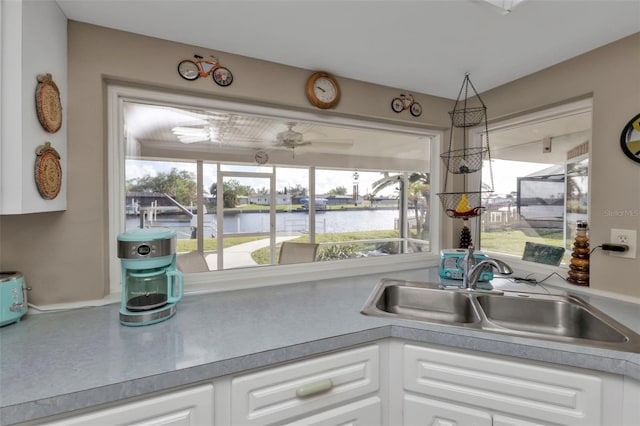 kitchen with a water view, white cabinetry, and sink