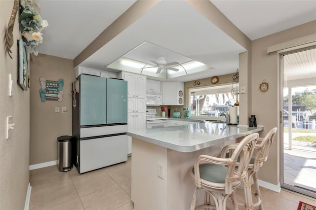 kitchen featuring kitchen peninsula, white appliances, light tile patterned floors, white cabinets, and a breakfast bar area