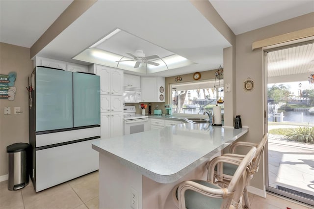 kitchen with kitchen peninsula, a water view, white appliances, a kitchen bar, and white cabinets