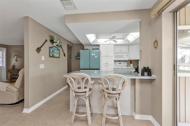 kitchen featuring kitchen peninsula, white appliances, white cabinets, a breakfast bar area, and light tile patterned flooring