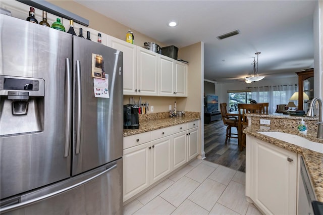 kitchen with light stone counters, sink, stainless steel fridge with ice dispenser, white cabinetry, and decorative light fixtures