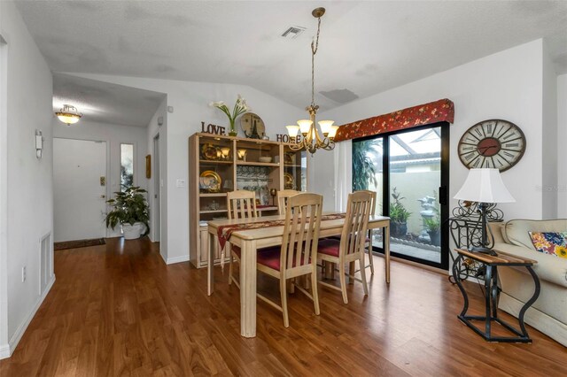 dining area with hardwood / wood-style floors, an inviting chandelier, and vaulted ceiling