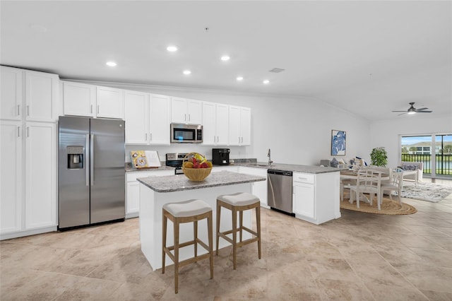 kitchen with a center island, ceiling fan, light stone countertops, appliances with stainless steel finishes, and white cabinetry