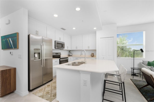 kitchen with appliances with stainless steel finishes, a breakfast bar, sink, a center island with sink, and white cabinetry