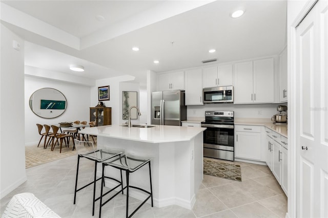 kitchen with appliances with stainless steel finishes, a kitchen island with sink, sink, white cabinetry, and a breakfast bar area