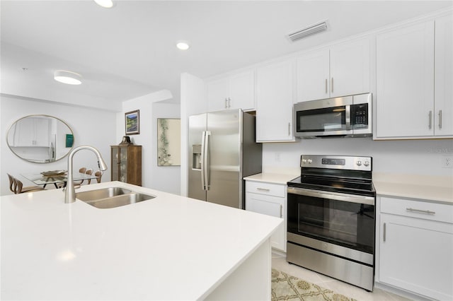 kitchen featuring appliances with stainless steel finishes, a kitchen island with sink, sink, light tile patterned floors, and white cabinets