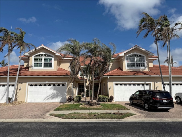 traditional home with decorative driveway, a garage, a tiled roof, and stucco siding