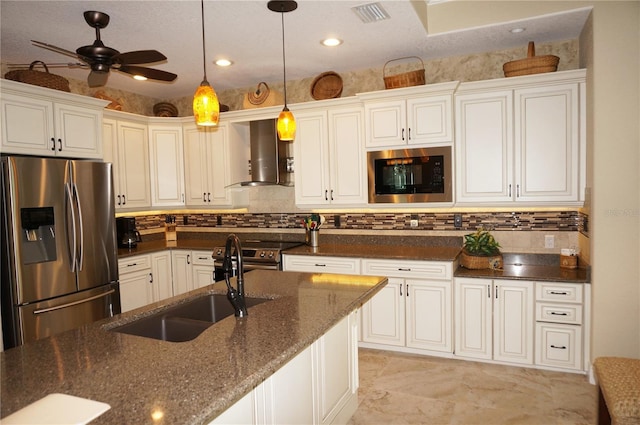 kitchen featuring stainless steel appliances, dark stone counters, wall chimney range hood, decorative light fixtures, and ceiling fan