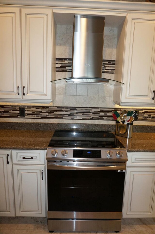 kitchen featuring stainless steel electric range, range hood, backsplash, dark stone counters, and white cabinetry