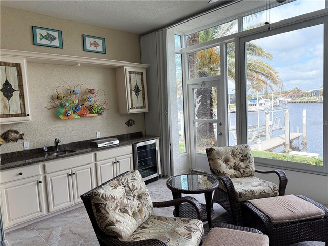 living area with wine cooler, a water view, plenty of natural light, a textured wall, and a textured ceiling