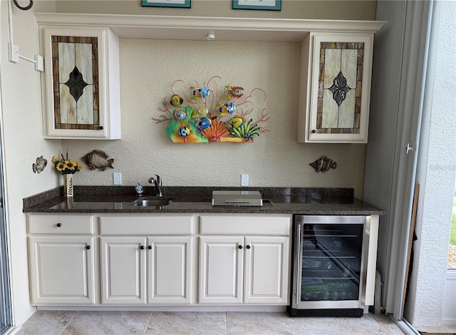 bar with white cabinets, beverage cooler, sink, and dark stone counters