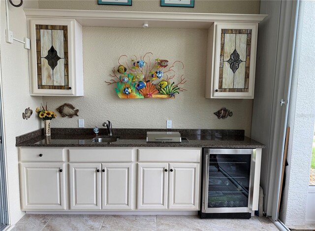 bar area with wine cooler, a sink, light tile patterned floors, and a textured wall