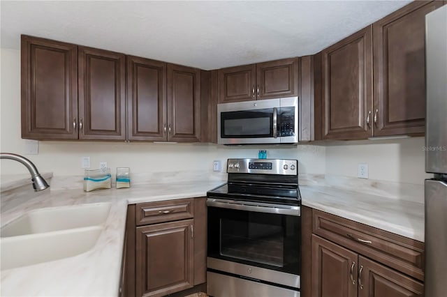 kitchen with a textured ceiling, dark brown cabinetry, stainless steel appliances, and sink