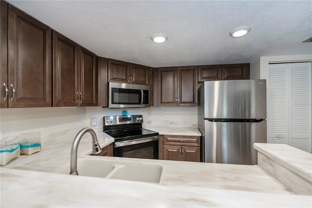 kitchen with dark brown cabinetry, sink, stainless steel appliances, and a textured ceiling