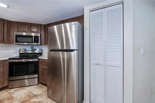 kitchen with dark brown cabinetry, a textured ceiling, and appliances with stainless steel finishes