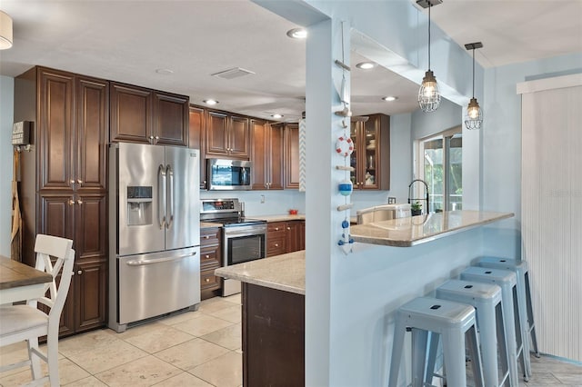 kitchen with stainless steel appliances, kitchen peninsula, a kitchen breakfast bar, light stone countertops, and decorative light fixtures