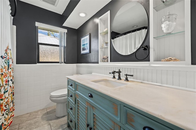 bathroom with toilet, vanity, and tile walls